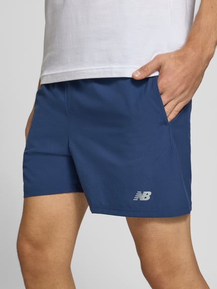 Männermodel trägt Shorts mit elastischem Bund und Logo von New Balance in Blau, Regular Fit, Detailaufnahme Nahaufnahme Oberschenkel.