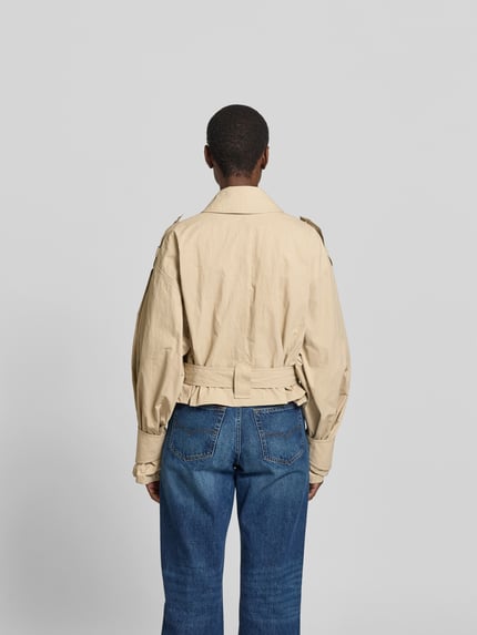 Frauenmodel trägt Jacke aus reiner Viskose Modell 'ZYNIA' von IRO in Beige mit Bindegürtel und Eingrifftaschen, lockere Passform, Ganzkörperansicht Rückansicht. Rückenlänge bei Größe 36: 52 cm, Brustweite 52 cm, Ärmellänge 61 cm.