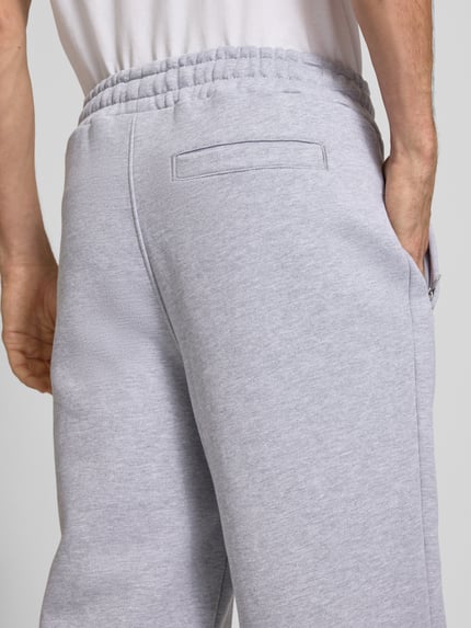 Männermodel trägt Loose Fit Sweatpants aus Baumwoll-Mix mit Label-Detail von PEGADOR in Hellgrau, sichtbare Eingrifftaschen, Detailaufnahme Rückansicht. Innenbeinlänge bei Größe M: 70 cm, elastischer Bund