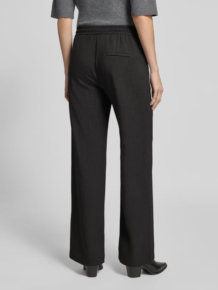 Frauenmodel trägt Regular Fit Hose mit elastischem Bund Modell 'Christy Clean' von MAC in Schwarz, Strukturmuster, Wide Leg, Ziertasche, Ganzkörperansicht Rückansicht.