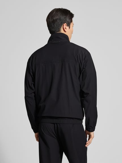 Männermodel trägt Regular Fit Trainingsanzug mit Label-Detail Modell 'LW_PS Spirit70 TT - PORSCHE X BOSS' von BOSS Green, unifarbenes Schwarz, elastische Abschlüsse, Stehkragen, Piqué-Material, Applikationen, Ganzkörperansicht Rückansicht.