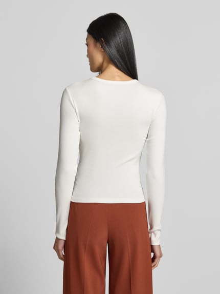 Frauenmodel trägt Slim Fit Langarmshirt aus Baumwoll-Mix Modell 'CHLOE' von VERO MODA in Weiß zu rostbraunen Hosen, Ganzkörperansicht Rückansicht. Damen Langarmshirt von VERO MODA.