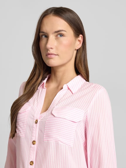 Modelka kobieca nosi Relaxed Fit Hemdbluse aus reiner Viskose Modell 'BUMPY' od Vero Moda, różowo-białe pionowe paski, dwie kieszenie na piersi, tekstura gładka, zbliżenie na górną część ciała.