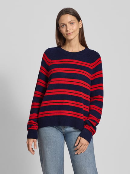 Vrouwenmodel draagt Loose Fit Strickpullover aus reinem Woll-Mix Modell 'LILIRIAA FINE STRIPES' van Armedangels, gestreept rood-blauw, grof gebreid, label patch, ronde hals, lange mouw, geribde boorden, allover-motief, vooraanzicht volledige lichaamsopname.