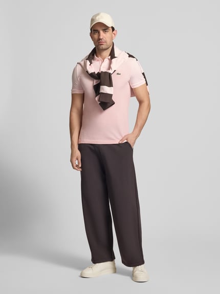 Männermodel trägt Slim Fit Poloshirt aus reiner Baumwolle von Lacoste, Optik: Unifarben, Logo-Stitching, Piqué, Ganzkörperansicht von vorne.