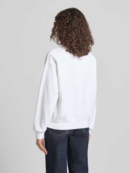 Frauenmodel trägt weißes Sweatshirt mit Label-Print Modell 'GRAPHIC' von Calvin Klein Jeans, lockere Passform, Rückansicht, Ganzkörperansicht.