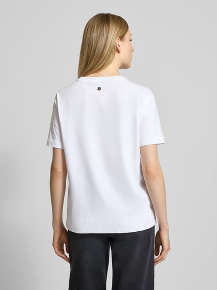 Frauenmodel trägt T-Shirt mit Ziersteinbesatz Modell 'Tammi' von JOOP!, weiße Baumwolle, Regular Fit, Rundhals, Ganzkörperansicht Rückansicht.