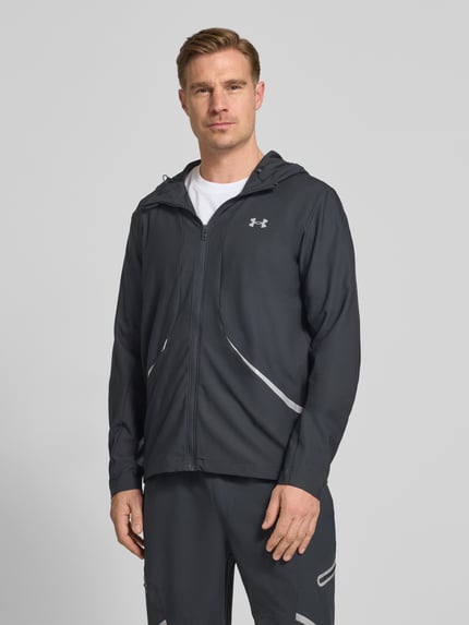 Męski model nosi Regular Fit Jacke mit Logo-Print Modell 'Unstoppable' od Under Armour z elastyczną mieszanką materiałów, czarny kolor, nadruk z logo, wpuszczane kieszenie zapinane na zamek błyskawiczny, zamek błyskawiczny, kaptur ze stójką, długość tyłu 74 cm, długość rękawów 68 cm; ujęcie: całkowity widok z przodu.