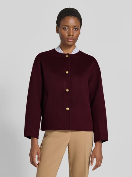 Frauenmodel trägt Relaxed Fit Kurzmantel aus Woll-Mix mit Kaschmir-Anteil von GANT, bordeaux, unifarben, goldene Knöpfe, seitliche Taschen, Rundhals, langarm, Ganzkörperansicht von vorne.
