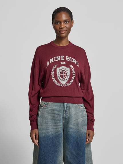 Frauenmodel trägt bordeauxrotes Sweatshirt mit Logo-Schriftzug Modell 'MIA SWEATER' von Anine Bing, Motiv-Print, Rundhals, Strick, Ganzkörperansicht von vorne.