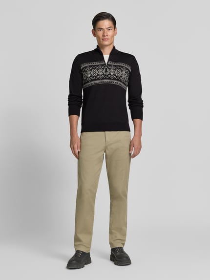 Männermodel trägt Wollpullover mit Label-Patch Modell 'Liaset' von Dale of Norway in Schwarz mit Muster, gerade geschnitten, Troyer-Kragen, reine Wolle, Ganzkörperansicht von vorne.