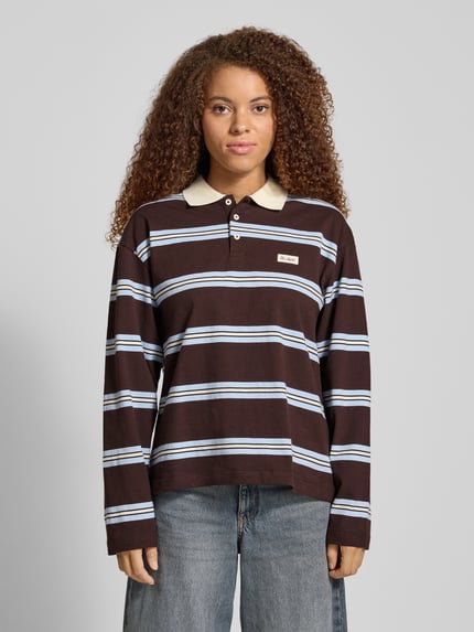 Frauenmodel trägt Relaxed Fit Poloshirt mit Label-Detail Modell 'Jolina' von OH APRIL, braun mit weißen Streifen, reine Baumwolle, Knopfleiste, Longsleeve, Ganzkörperansicht von vorne.