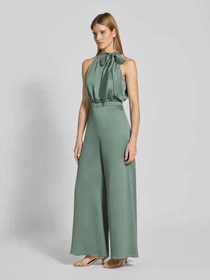Frauenmodel trägt Jumpsuit mit Schleifen-Detail von SWING in grün, Regular-Fit, Neckholder, leicht glänzende Oberfläche, Ganzkörperansicht von vorne, Rückenlänge bei Größe 36: 40 cm, Brustweite bei Größe 36: 36 cm, Gesamtlänge bei Größe 36: 152 cm, Innenbeinlänge bei Größe 36: 83 cm, rückseitiger Reißverschluss.