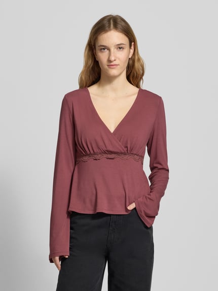Frauenmodel trägt Slim Fit Langarmshirt aus Viskose-Mix Modell 'SINI' von Only in Wickeloptik, tiefes V, Spitze, Ganzkörperansicht von vorne.