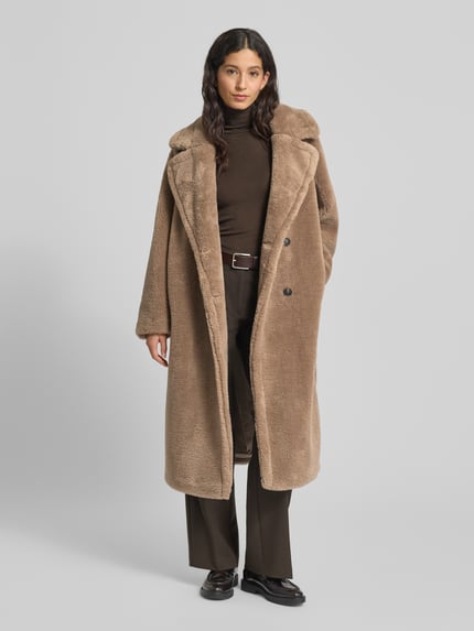 Vrouwenmodel draagt Mantel uit Teddyfell van Smith and Soul in los model met reverskraag en knoopsluiting, kleur beige, Ganzkörperansicht von voren. Ruglengte maat S 115 cm, schouderbreedte 44 cm, borstwijdte 62 cm, mouwlengte 62 cm.
