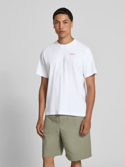 Mężczyznamodel nosi Regular Fit T-Shirt mit Statement-Print von Forét z bawełny, okrągły dekolt, krótki rękaw, długość tyłu w rozmiarze M: 67 cm, widok całej sylwetki z przodu