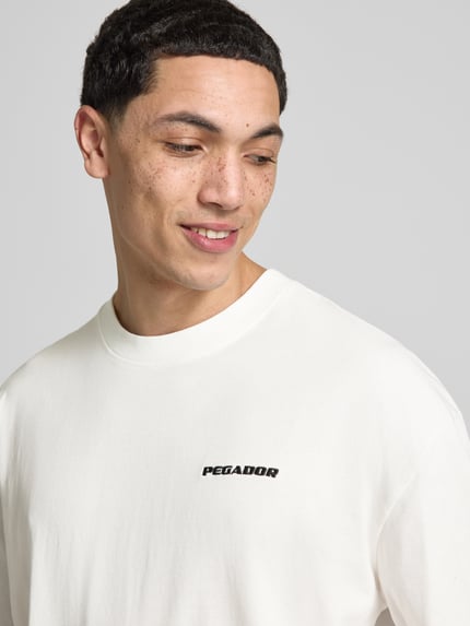 Męski model nosi Oversized T-Shirt mit Logo-Stitching od Pegador, czysta bawełna, krój oversized fit, okrągły dekolt, długość tyłu w rozmiarze M: 73 cm, zbliżenie na górną część ciała