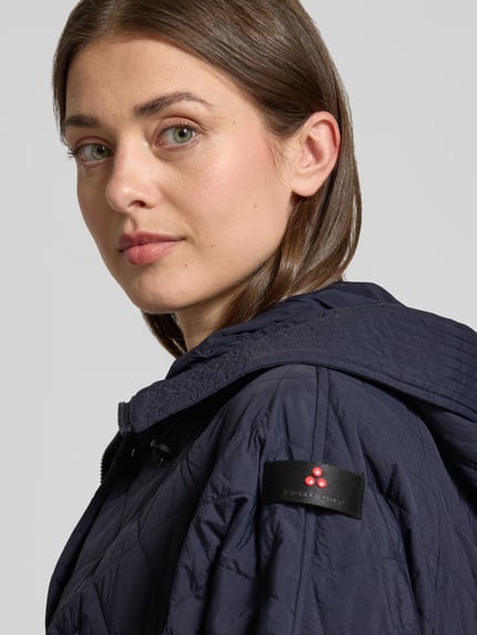Frauenmodel trägt Relaxed Fit Jacke in Stepp-Optik Modell 'Texel' von Peuterey, dunkelblau, Stehkragen, Pattentaschen, Tunnelzug in der Taille, Nahaufnahme Oberkörper. Rückenlänge bei Größe 38: 80 cm, Schulterbreite: 50 cm, Brustweite: 72 cm, Ärmellänge: 59 cm.