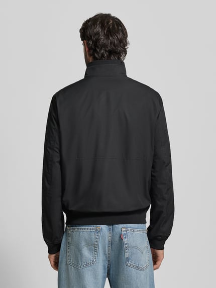 Männermodel trägt Regular Fit Jacke mit Stehkragen von MCNEAL w kolorze czarnym, elastyczne wykończenia, wpuszczane kieszenie na zamek błyskawiczny, długość tyłu w rozmiarze M: 64 cm, szerokość ramion w rozmiarze M: 43 cm, szerokość w rozmiarze M: 55 cm, długość rękawów w rozmiarze M: 67 cm, widok całej sylwetki z tyłu