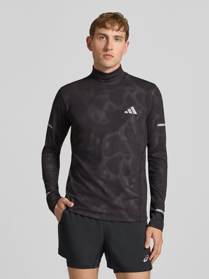 Mężczyzna model nosi Slim Fit Sport-Langarmshirt mit reflektierenden Details von adidas Training, czarny kolor, matowa i błyszcząca tekstura, Ganzkörperansicht von vorne.