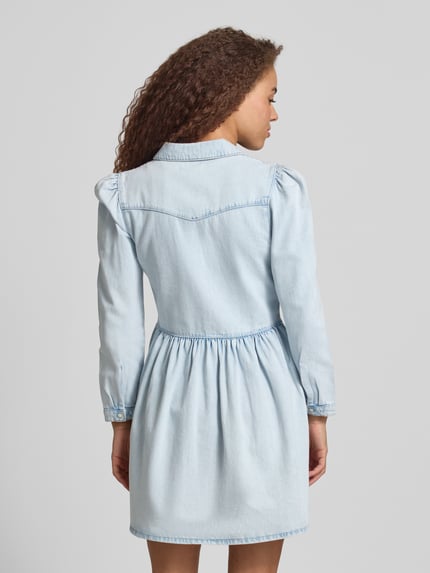 Frauenmodel trägt Mini-Jeanskleid aus reiner Baumwolle Modell 'CYRUS' von Only in heller Denim-Optik mit Knopfleiste, Ganzkörperansicht Rückansicht.