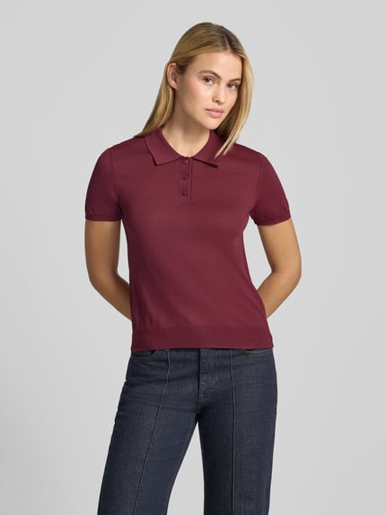 Frauenmodel trägt Poloshirt aus Viskose-Mix Modell 'LUXEN' von MANGO, tailliert, bordeauxrot, glatte Textur, Ganzkörperansicht von vorne.