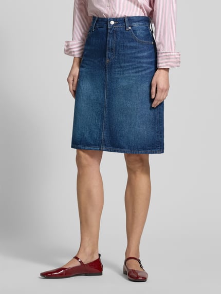 Frauenmodel trägt Körpernaher Jeansrock aus reiner Baumwolle von Tommy Hilfiger, Optik: Unifarben, Passform: Körpernah, Länge: Knielang, Label-Patch, Logo-Detail, Nieten, Gürtelschlaufen, Verschluss: Knopf und Reißverschluss, 5-Pocket-Design, Materialverarbeitung: Denim, aus Baumwolle, Ganzkörperansicht von vorne.
