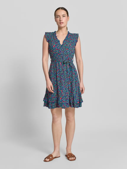 Frauenmodel trägt Minikleid aus Viskose mit Bindegürtel von Apricot in Blau mit Blumenmuster, Rüschen, Schmetterlingsärmel, Stufenrock, taillierter Schnitt, V-Ausschnitt, Knopfleiste, Rückenlänge 70 cm, Brustweite 47 cm, Ganzkörperansicht von vorne.