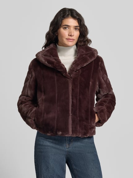 Kobiece modelka ma na sobie kurtkę z sztucznego futra Jacke aus Kunstfell Modell 'NEW SOPHY' od GUESS, krój regular fit, wykładany kołnierz, długość tyłu w rozmiarze S: 58 cm, szerokość ramion w rozmiarze S: 42 cm, szerokość w rozmiarze S: 52 cm, długość rękawów w rozmiarze S: 62 cm, widok na górną część ciała z przodu.