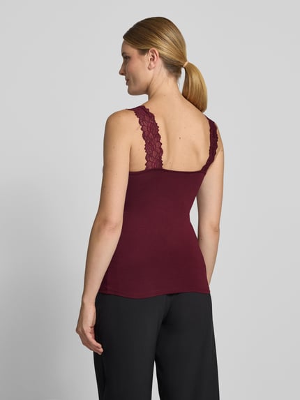 Frauenmodel trägt bordeauxrotes Slim Fit Tanktop aus Viskose-Mix Modell 'ROSA' von VERO MODA, schwarze Hose, Ganzkörperansicht Rückansicht.