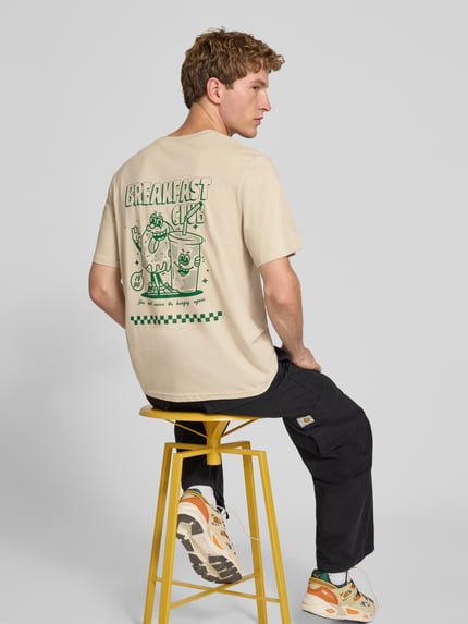 Męski model nosi Regular Fit T-Shirt aus reiner Baumwolle Modell 'BREWY' od JACK & JONES w kolorze jasnobeżowym z nadrukiem z napisem, miękka gładka struktura, Długość tyłu w rozmiarze M: 68 cm, Ganzkörperansicht Rückansicht.