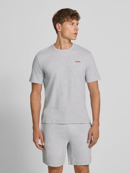 Männermodel trägt Herren T-Shirt aus Baumwoll-Mix Modell 'AUSTIN' von HUGO in Hellgrau mit feiner Struktur, Ganzkörperansicht von vorne.