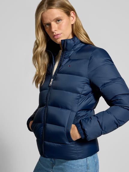 Frauenmodel trägt Regular Fit Daunenjacke mit Kunstfell von Tommy Jeans in Dunkelblau, glatte Oberfläche, Ganzkörperansicht von vorne. Damen Daunenjacke von Tommy Jeans.