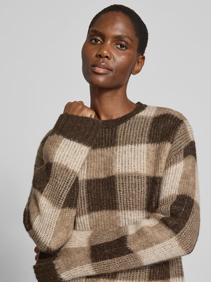 Frauenmodel trägt Pullover aus Wolle Alpaka-Mix von SELECTED in mehrfarbiger Strickoptik mit kariertem Muster, Rundhals und langen Ärmeln, Nahaufnahme Oberkörper.