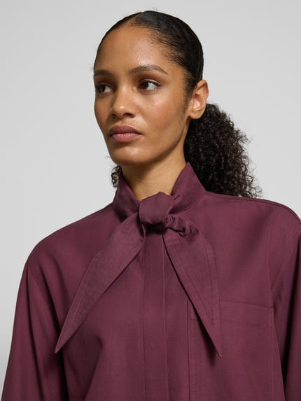 Vrouwenmodel draagt Hemdbluse met Brusttasche van JAKE*S STUDIO WOMAN in bordeaux, Lyocell-katoenmix, losse pasvorm, strikdetail, borstzak, verborgen knopensluiting, Nahaufnahme bovenlichaam.