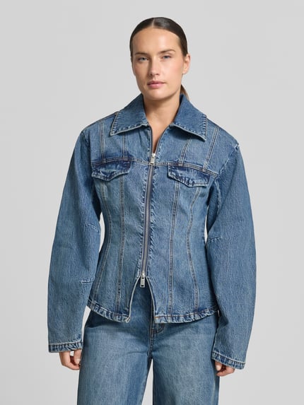 Frauenmodel trägt Jeansjacke aus Baumwoll-Mix Modell 'Melu' von Gestuz in Blau mit Zweiwege-Reißverschluss, Nahaufnahme Oberkörper.