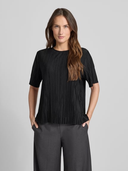 Frauenmodel trägt Relaxed Fit Kurarzm Bluse mit Rundhalsausschnitt Modell 'Uma' von Samsøe Samsøe, Schwarz mit feiner Plissee-Struktur, elastischer Material-Mix, Ganzkörperansicht von vorne.