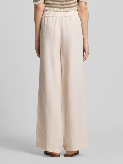 Frauenmodel trägt Leinenhose mit elastischem Bund Modell 'Roma' von STEHMANN, beige Farbe, Wide-Leg-Pants, Ganzkörperansicht Rückansicht.