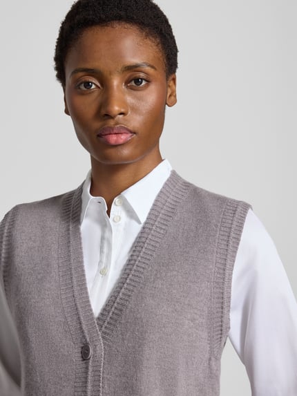 Vrouwenmodel draagt Strickweste mit Kaschmir-Anteil van windsor., Mix van scheerwol en kasjmier, regular fit, V-hals, knoopsluiting, strookzakken, ribboorden, ruglengte 53 cm bij maat 36, kleur lichtgrijs, textuur zacht en geribd. Nahaufnahme bovenlichaam.