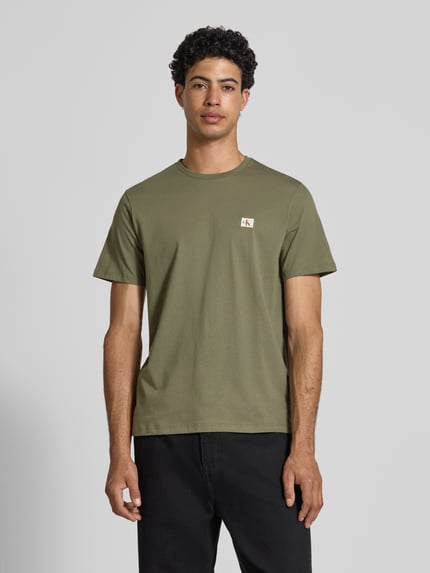 Mannenmodel draagt Regular Fit T-Shirt aus reiner Baumwolle van Calvin Klein Jeans in effen kaki, ronde hals, korte mouwen, label patch, katoenstructuur, regular fit. Ganzkörperansicht van voren.