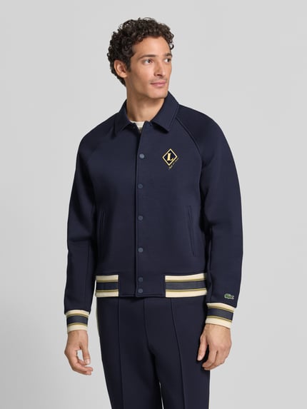 Mężczyzna nosi Regular Fit Sweatjacke aus Baumwoll-Mix von Lacoste, granatowa, detale żółte i białe, bluza rozpinana, Ganzkörperansicht z przodu.