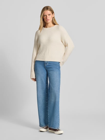 Frauenmodel trägt Relaxed Fit Strickpullover mit elastischen Abschlüssen von REVIEW, lockere Passform, beige Farbe, Jeans, Ganzkörperansicht von vorne.