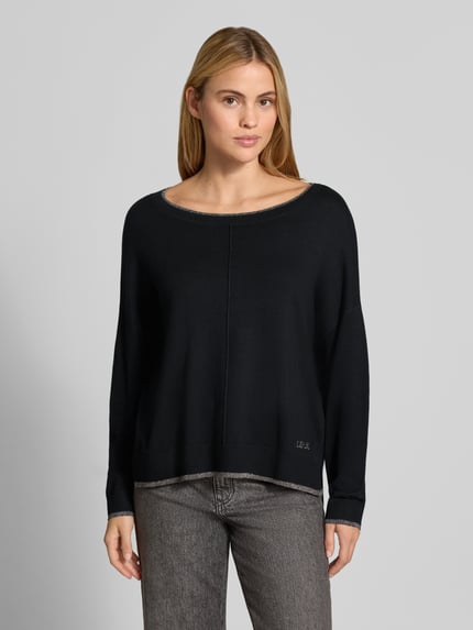 Vrouwenmodel draagt Relaxed Fit pullover uit viscosemix Model 'MAGLIA CHIUSA' van Liu Jo White, zwart, tricotlook, logodetail, Ganzkörperansicht von voren. Context: Dames pullover van Liu Jo White, viscosemix, relaxed fit, model 'MAGLIA CHIUSA', verlengde achterkant, tricotlook, logodetail, ruglengte bij maat S: 58 cm, mouwlengte bij maat S: 46 cm.