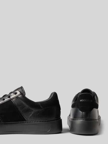 Produktfoto, Sneaker aus echtem Leder Modell 'Classic Court' von Woolrich in Schwarz mit strukturierter Sohle und Kontrastbesatz, seitliche und Rückansicht, Herren Sneaker, abgerundete Form, Schnürverschluss, Label-Schriftzug, Absatzhöhe 4 cm, Schafthöhe 8 cm, Schaftweite 9 cm.