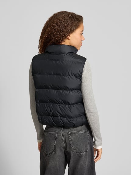 Frauenmodel trägt Steppweste mit Stehkragen Modell 'BOSTON PUFFER VEST' von NEW BALANCE, unifarben, Struktur, Ganzkörperansicht Rückansicht.