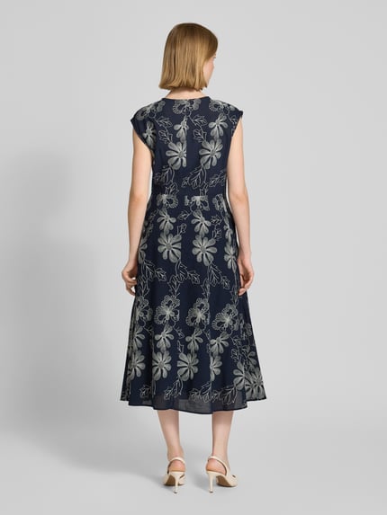 Frauenmodel trägt Midikleid mit Stitchings und Eingrifftaschen von Milano Italy, dunkelblauer Baumwoll-Mix mit floralen Nähten, A-Linie, Ganzkörperansicht Rückansicht.