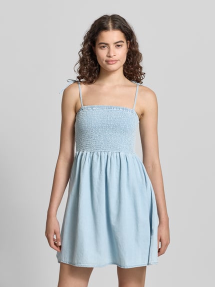Frauenmodel trägt Damen Minikleid mit Smok-Detail von Noisy May aus Reine Baumwolle in Denim-Optik, A-Linie, Träger mit Schnürung, Ganzkörperansicht von vorne. Modell 'OREGON', Rückenlänge bei Größe S: 68 cm, Brustweite bei Größe S: 35 cm.