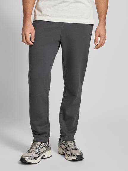 Męski model nosi Sweatpants mit elastischem Bund od CHAMPION, bawełniany miks, luźny krój, elastyczny pas, szare, z przodu, zbliżenie na dolną część ciała.