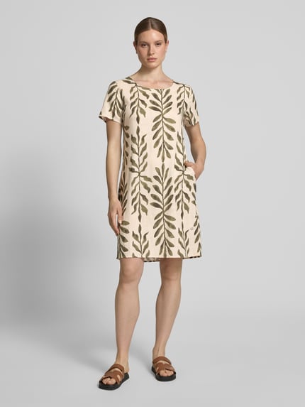 Kobiece model nosi Relaxed Fit sukienkę z mieszanki wiskozy model 'Tara' od ZABAIONE, beż z zielonym wzorem liści, okrągły dekolt, z krótkim rękawem, długość tyłu w rozmiarze S: 96 cm, szerokość w rozmiarze S: 49 cm, długość rękawów w rozmiarze S: 21 cm, całkowity widok z przodu.
