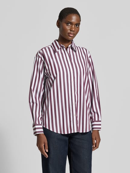 Frauenmodel trägt Relaxed Fit Langarmbluse aus reiner Baumwolle von GANT, breite bordeauxrote und weiße Streifen, Ganzkörperansicht von vorne.
